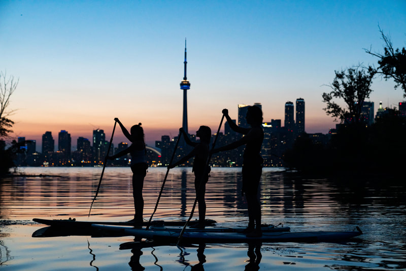 3 Paddlers after a relaxing SUP Yoga session. They enjoy that last bits of sunlight and the city lights slowly turning on before heading back home.